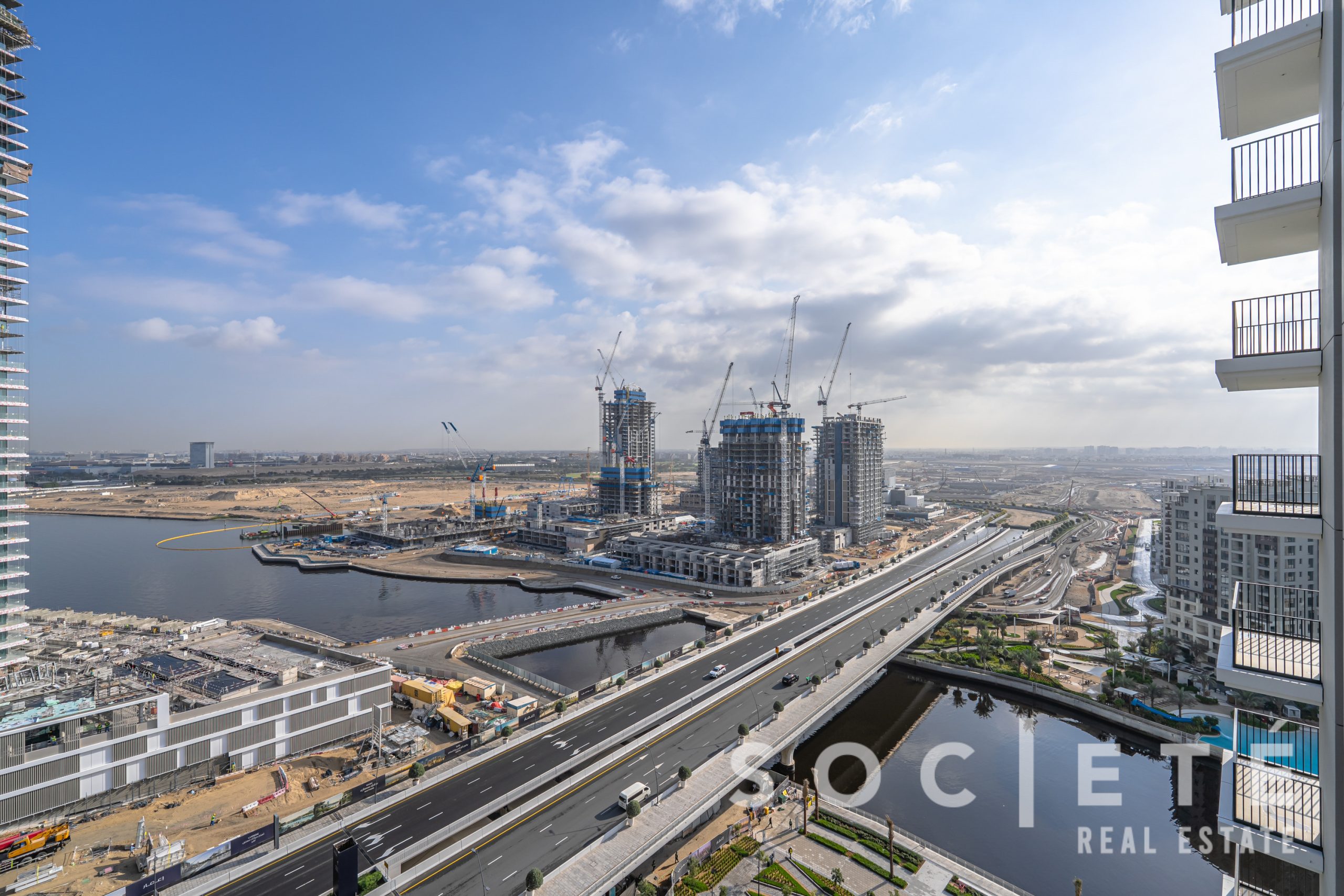 Wide view of a coastal construction site with cranes and high-rise buildings under construction beside a highway.