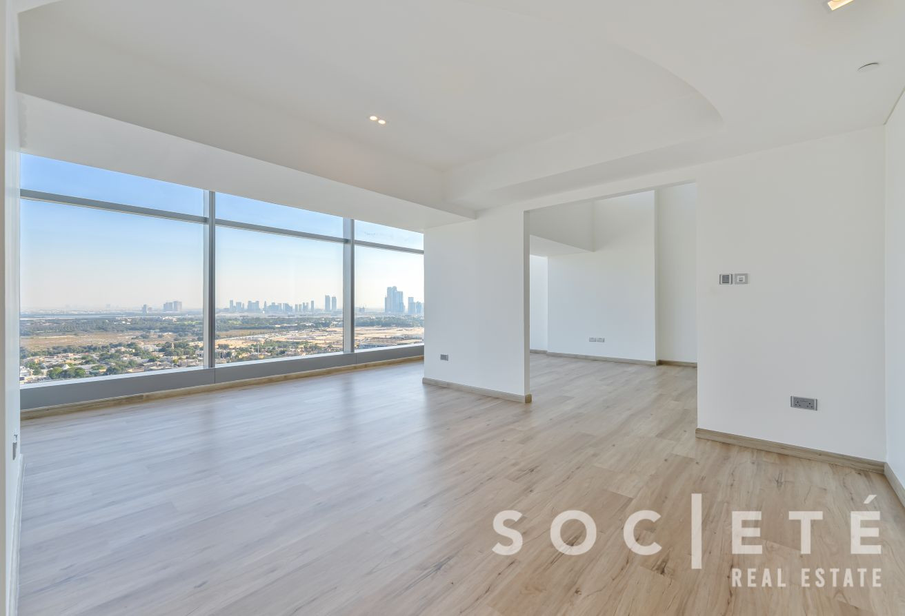 Empty modern living space with large floor-to-ceiling windows and a panoramic city skyline view; light wood flooring and white walls.