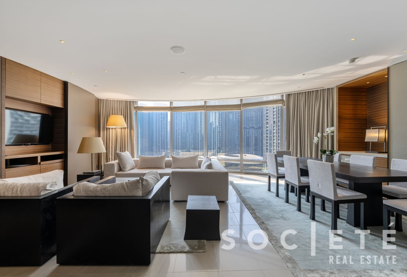 Spacious modern living and dining area with large curved windows overlooking a city skyline.
