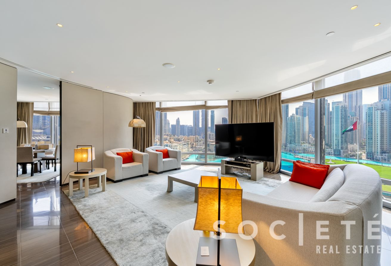 Bright modern living room with cream sofas, orange cushions, and a wall of windows overlooking a city skyline and marina view on the right.
