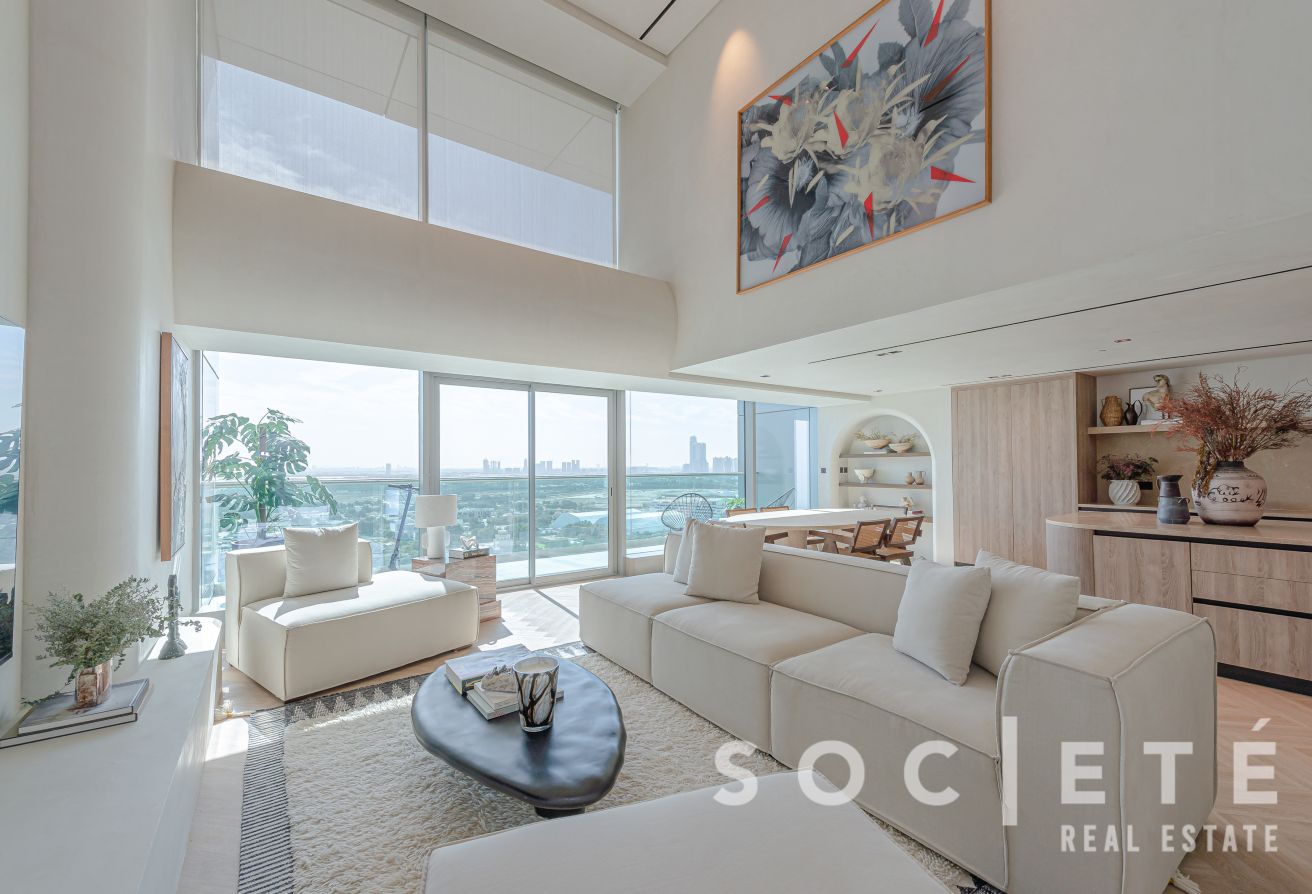 Bright open-plan living room with a cream sectional, glass walls, and a city skyline view.